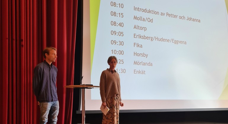 Två personer står på scen och håller i en presentation.