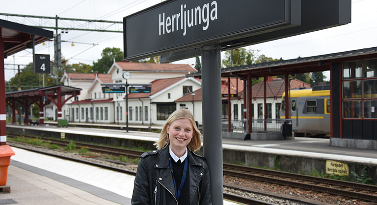 Person som står vid en järnvägsstation där det står Herrljunga på en skylt.. 