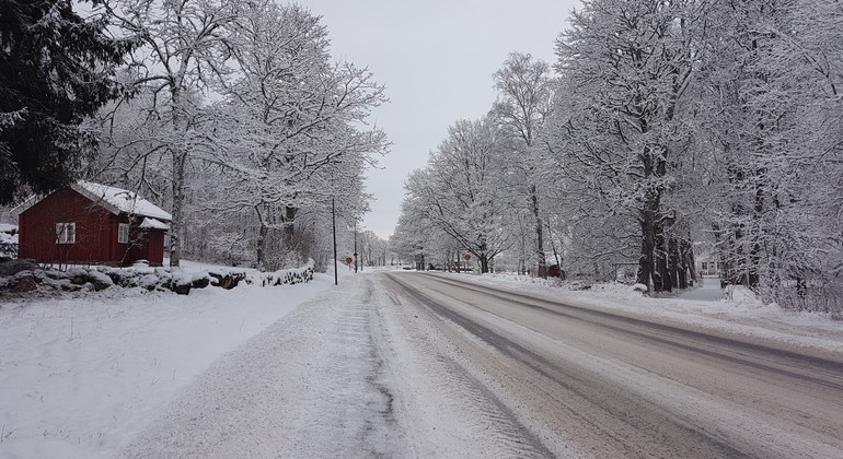 En väg täckt med snö och ett rött hus ligger till vänster