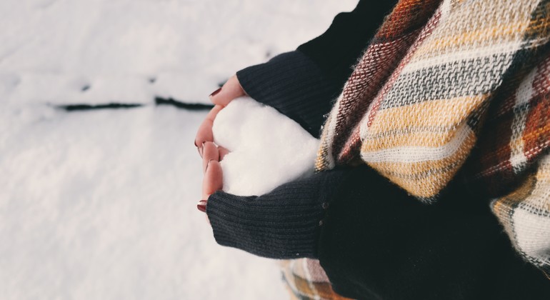 Händer som håller om en snöboll formad som ett hjärta.