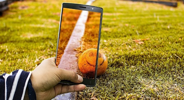 En person fotar en orange boll med en smiley och en järnvägsräls med en mobiltelefon