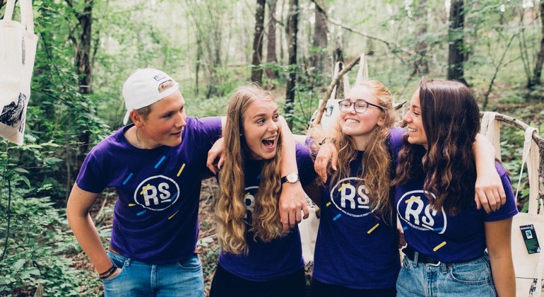 Foto visar 4 ungdomar i lila t-shirts, de står i en skog